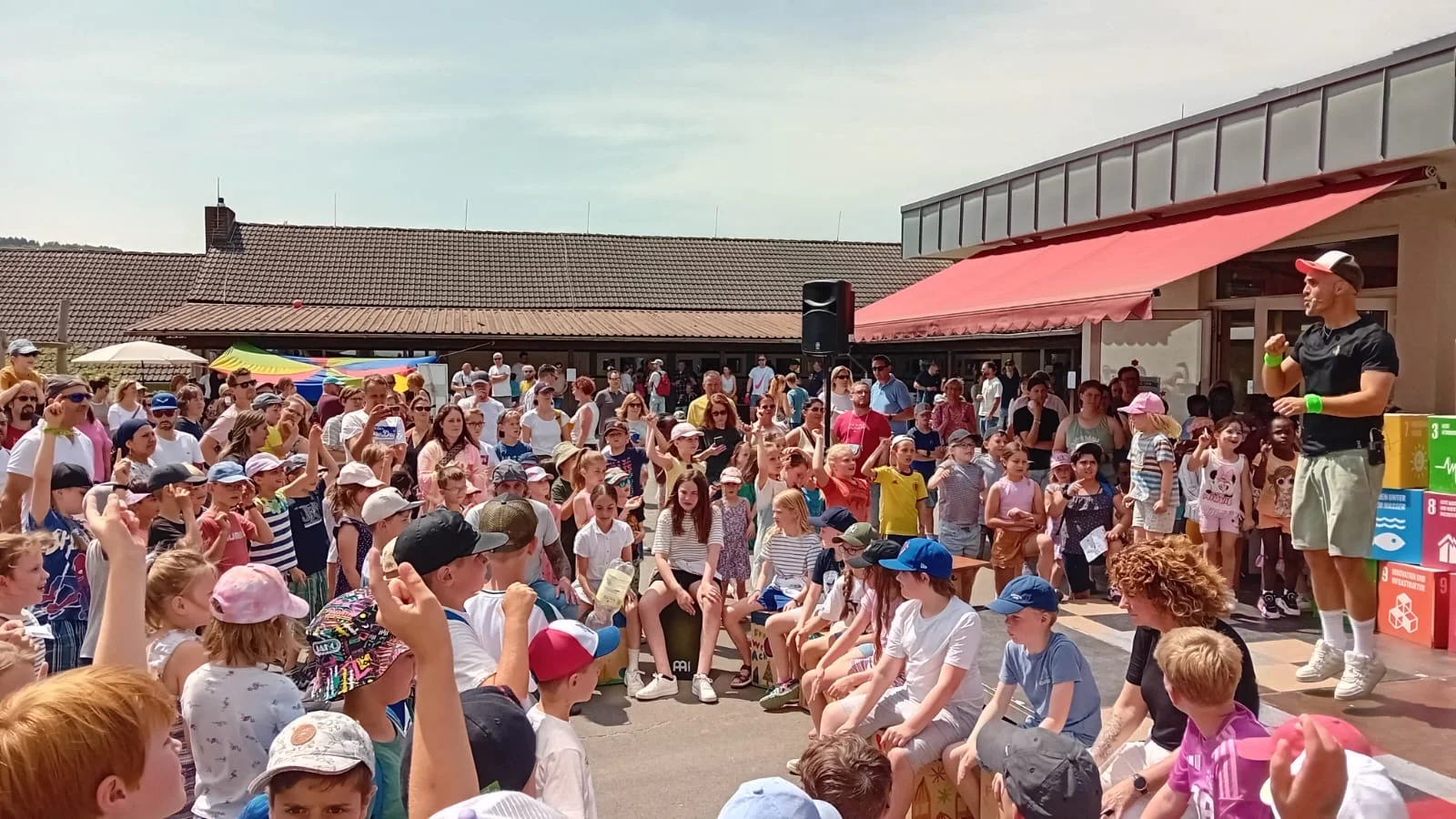 Norbert Klotz auf der Bühne beim Schulfest vor einer großen Menge Kinder mit erhobenen Händen